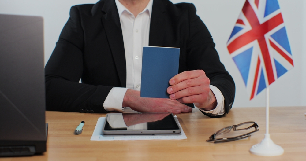 7 Things to Avoid During the UK Visa Application Process: British embassy man officer showing passport immigrant, work visa, citizenship.
