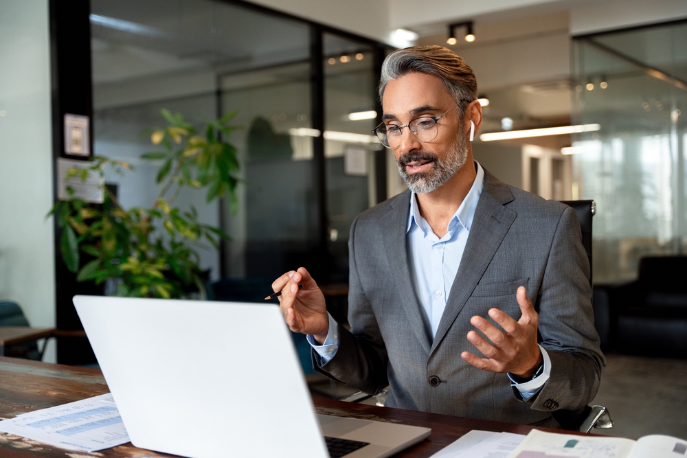 Top 10 Fully Remote, In-Demand Jobs That Pay Over $100K: Happy mature manager looking at laptop in office. Busy middle aged professional business man executive investor ceo leader using computer working with online finances sitting at desk.